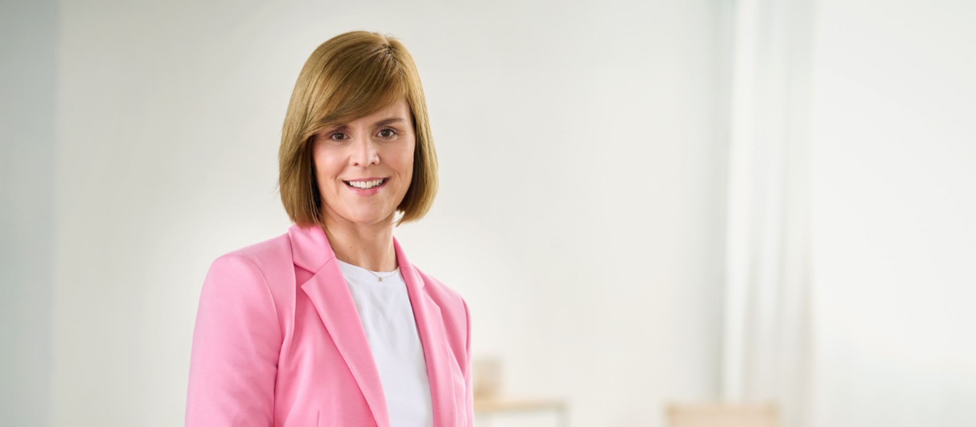 Eva Griewel, femme dans une pièce lumineuse, vêtue d’un blazer rose et d’une chemise blanche