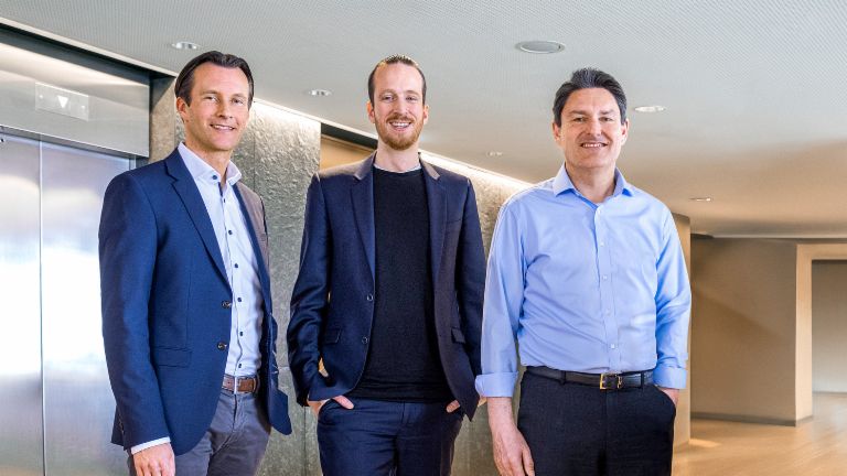 Trois membres masculins du conseil d'administration du Groupe EOS se tiennent en tenue professionnelle devant des ascenseurs dans un cadre moderne.