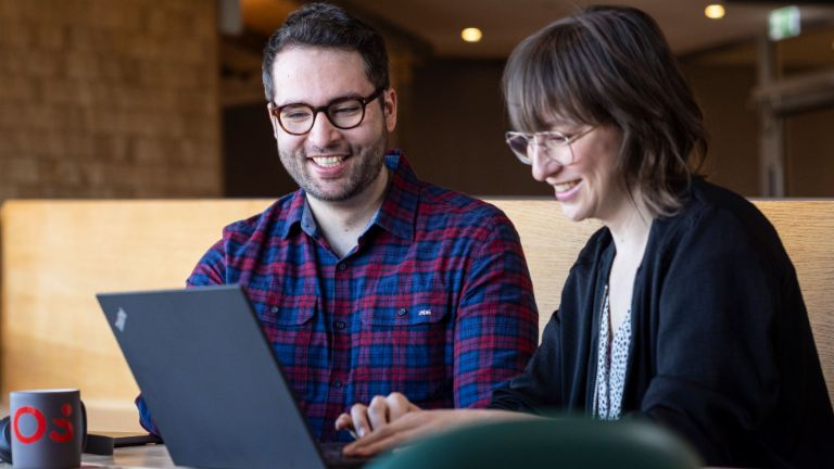 Deux collaborateurs d'EOS regardent ensemble un ordinateur portable tout en étant absorbés par une conversation.