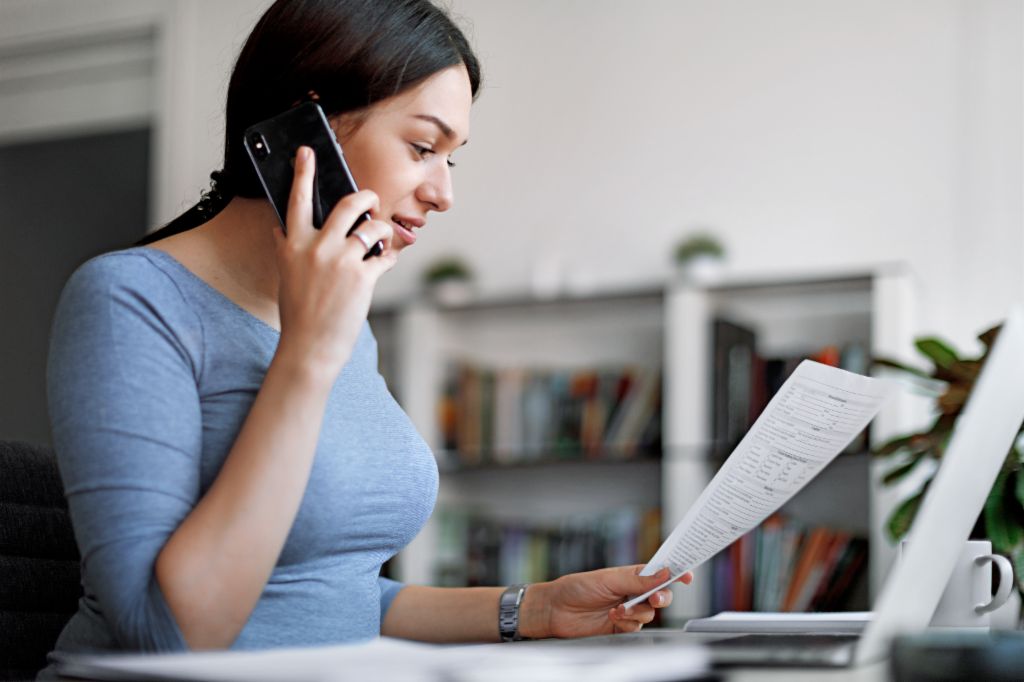 Femme en haut bleu sur un téléphone portable tout en tenant une facture dans ses mains