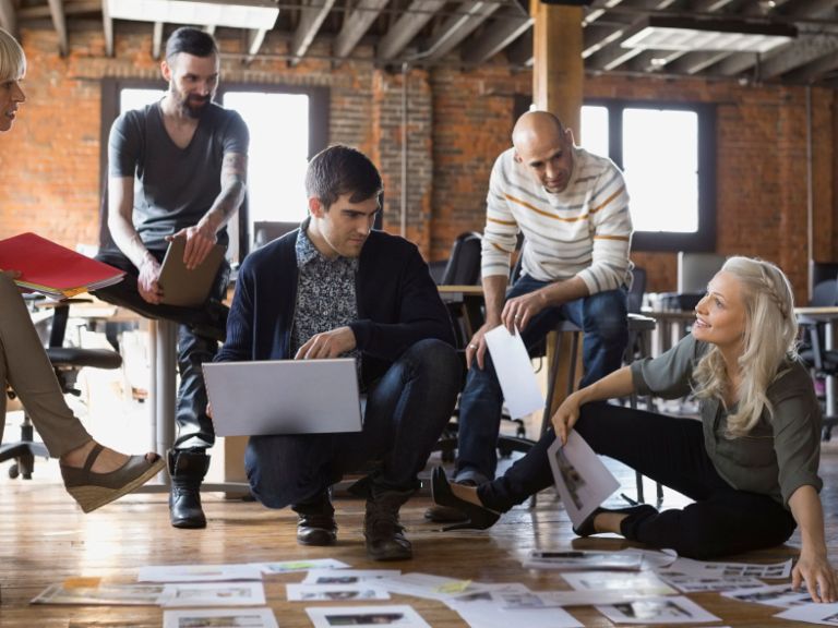Agiles Arbeiten: Eine Gruppe von Mitarbeiterinnen und Mitarbeitern diskutiert über Zetteln auf dem Boden.