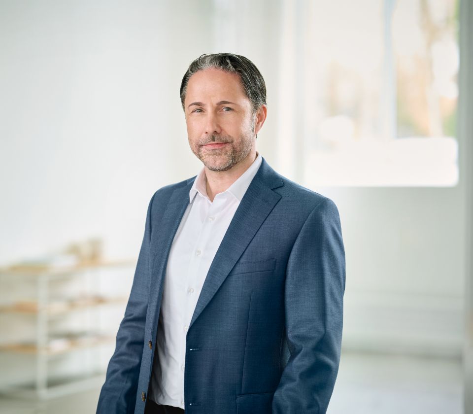Portrait von Marwin Ramcke, Vorsitzender der Geschäftsführung der EOS Gruppe in einem hellen Raum und trägt ein dunkles Sakko