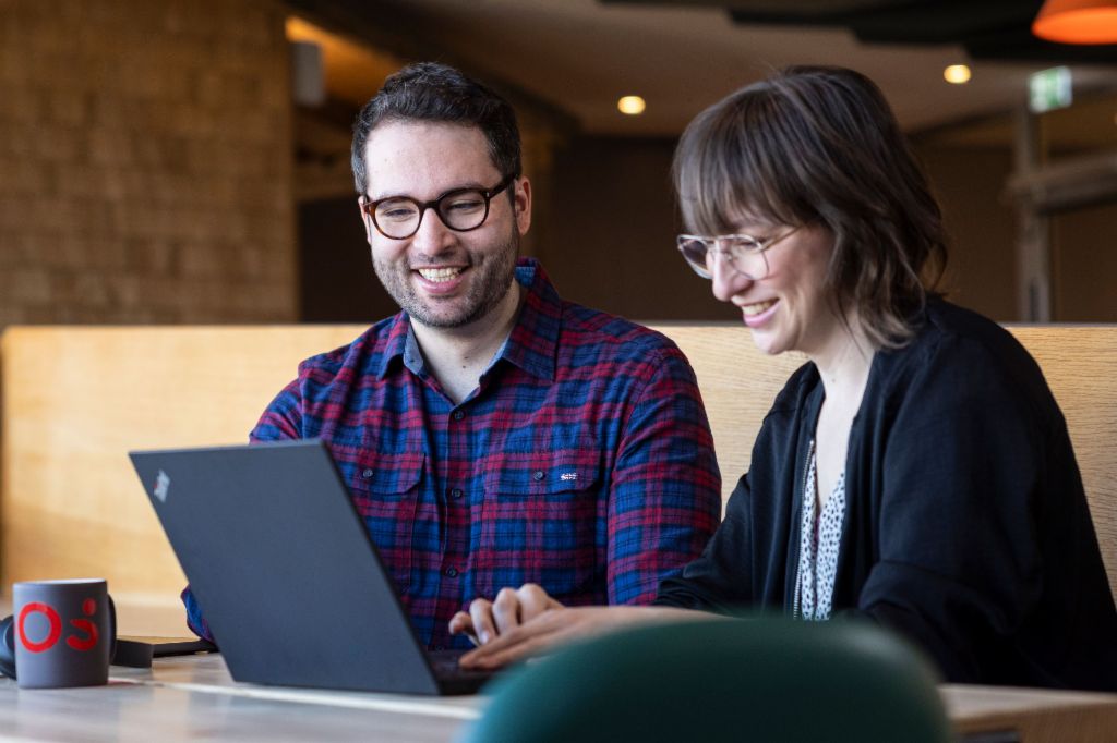 Two EOS employees look at a laptop together while engrossed in a conversation.
