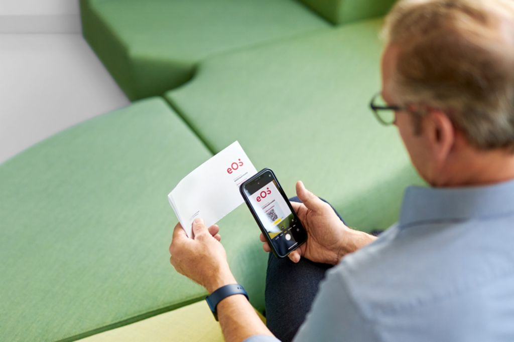 Ein Mann scannt einen QR-Code auf einem Brief von EOS mit seinem Smartphone, um seine offene Forderung online auf EOS Portal zu begleichen.