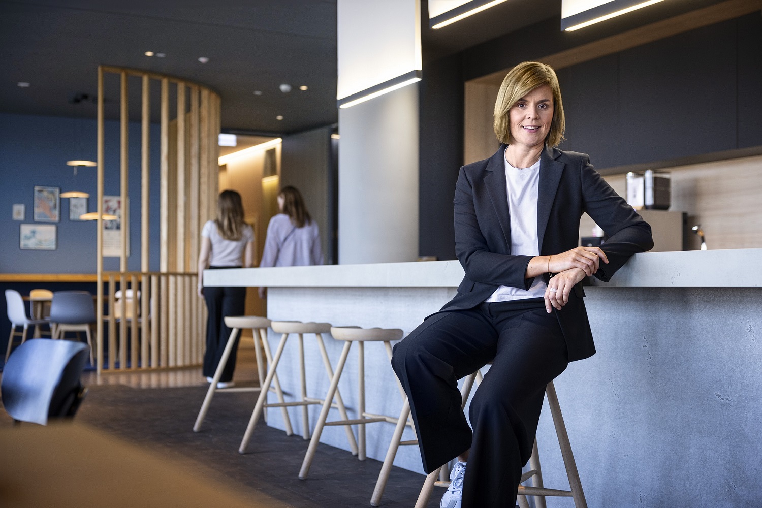 Dr. Eva Griewel, CFO der EOS Gruppe, sitzt in einem Social Space auf einem Hochstuhl und trägt einen schwarzen Blazer.