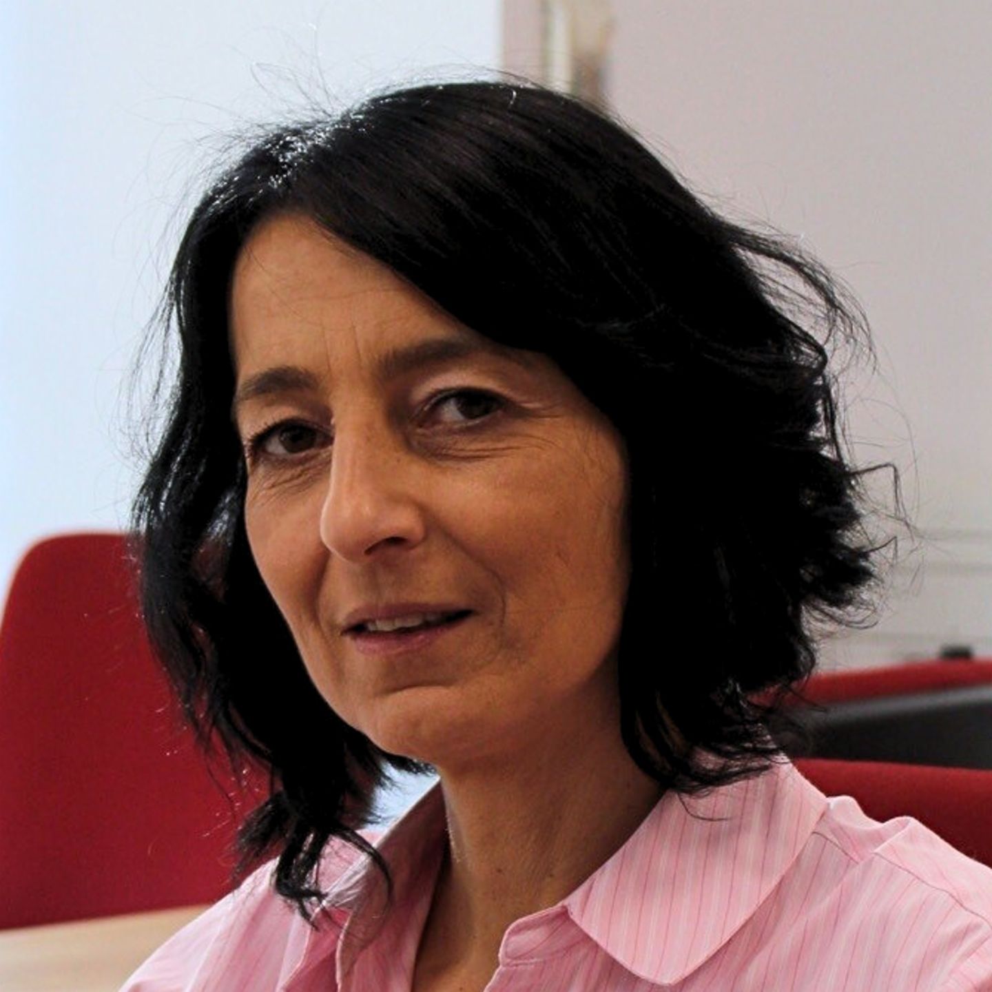 Cristina Pasere, Managerin Compliance Operations Support, EOS in Rumänien Cristina Pasere, Managerin Compliance Operations Support, EOS Rumänien sitzt in rosa gestreifter Bluse am Schreibtisch und guckt in die Kamera