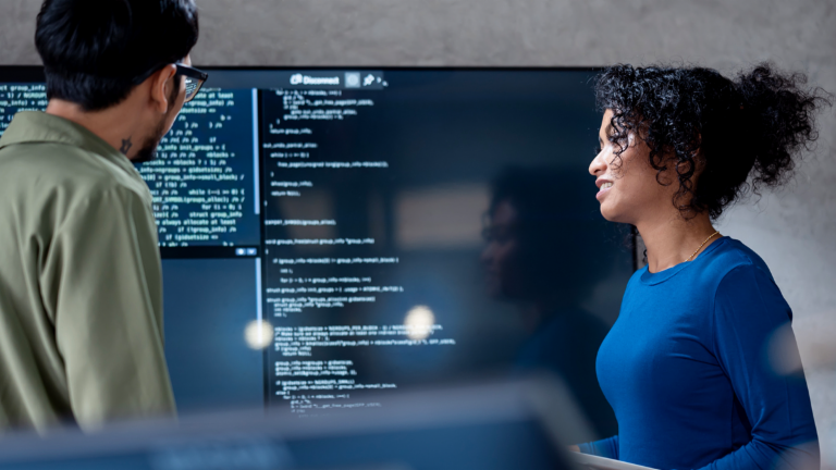 KI im Forderungsmanagement: In diesem Bild analysieren zwei Fachleute gemeinsam Programmiercode für automatisierte Prozesse auf einem großen Bildschirm. Die Szene veranschaulicht die praktische Anwendung von Künstlicher Intelligenz (KI) und Robotic Process Automation (RPA) im Forderungsmanagement – ein Beispiel für die digitale Transformation im Forderungsmanagement.