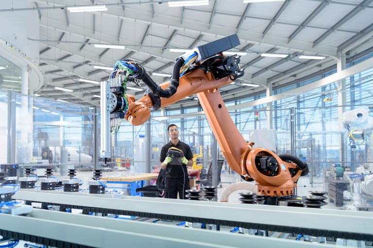 Künstliche Intelligenz und Recht: Ein Industrieroboter wird von einem Menschen programmiert. Künstliche Intelligenz und Recht: Ein Industrieroboter wird von einem Menschen programmiert.