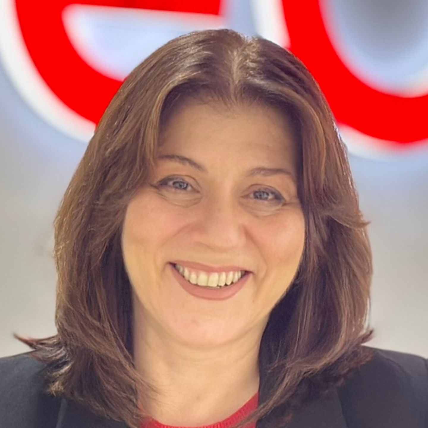 Belén Barreiro, agente du centre de contact chez EOS en Espagne, est appuyée contre un comptoir dans un blazer noir devant un logo EOS lumineux.
