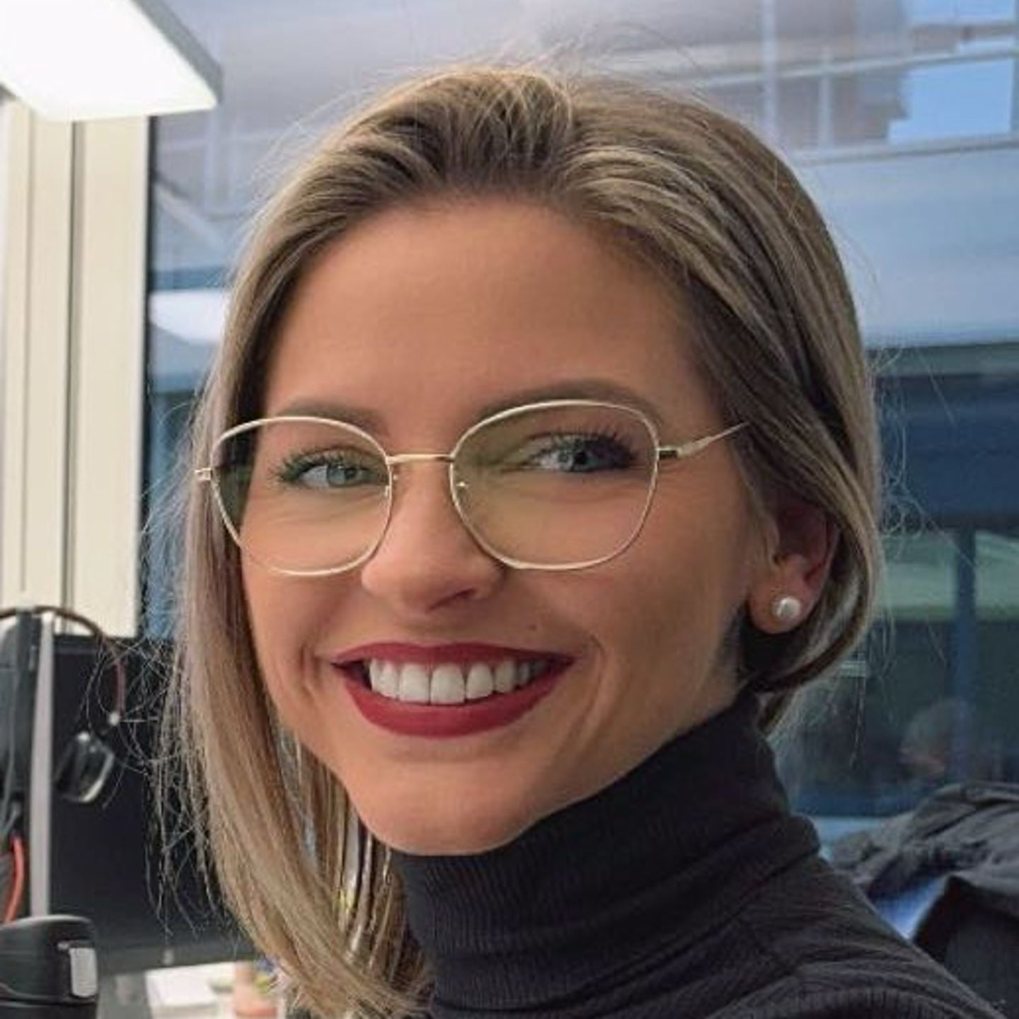 Genny Bollinger, spécialiste en restructuration de la dette chez EOS en Suisse, est assise à son bureau, vêtue d'un pull à col roulé gris, et sourit à la caméra.