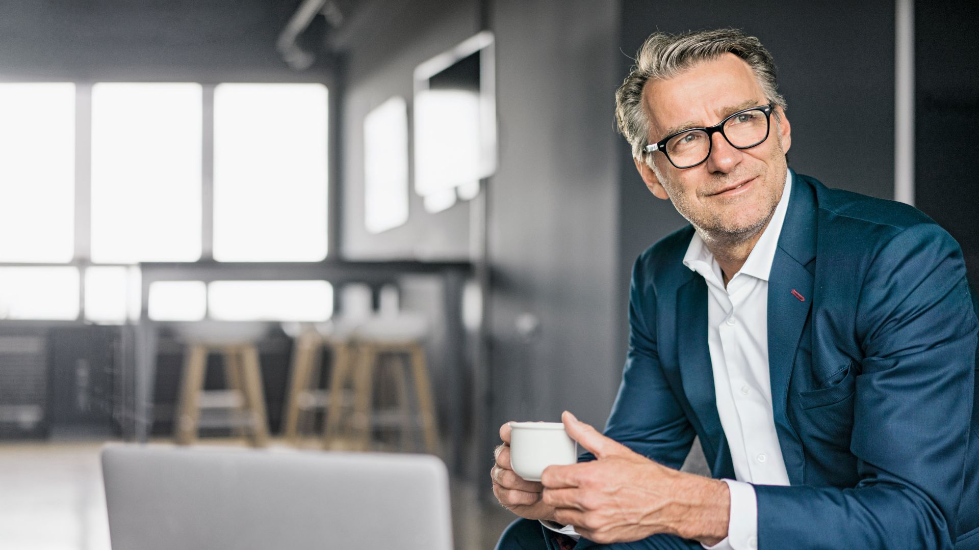 Portrait d'un homme d'affaires mûr assis, portant un costume bleu et tenant une tasse de café blanche