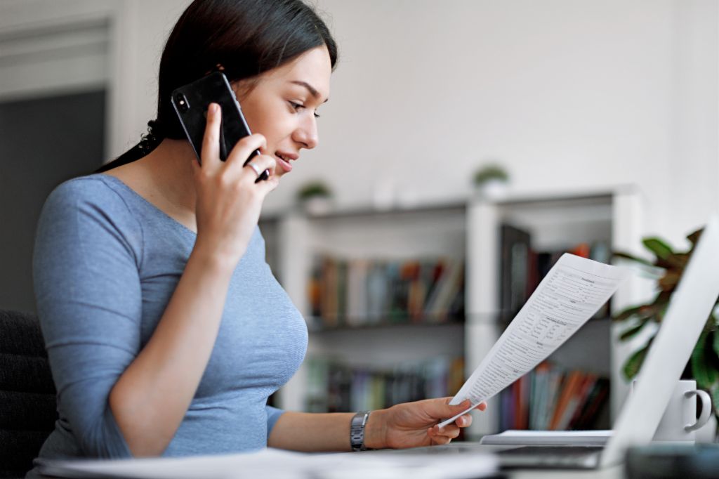 Femme en haut bleu sur un téléphone portable tout en tenant une facture dans ses mains